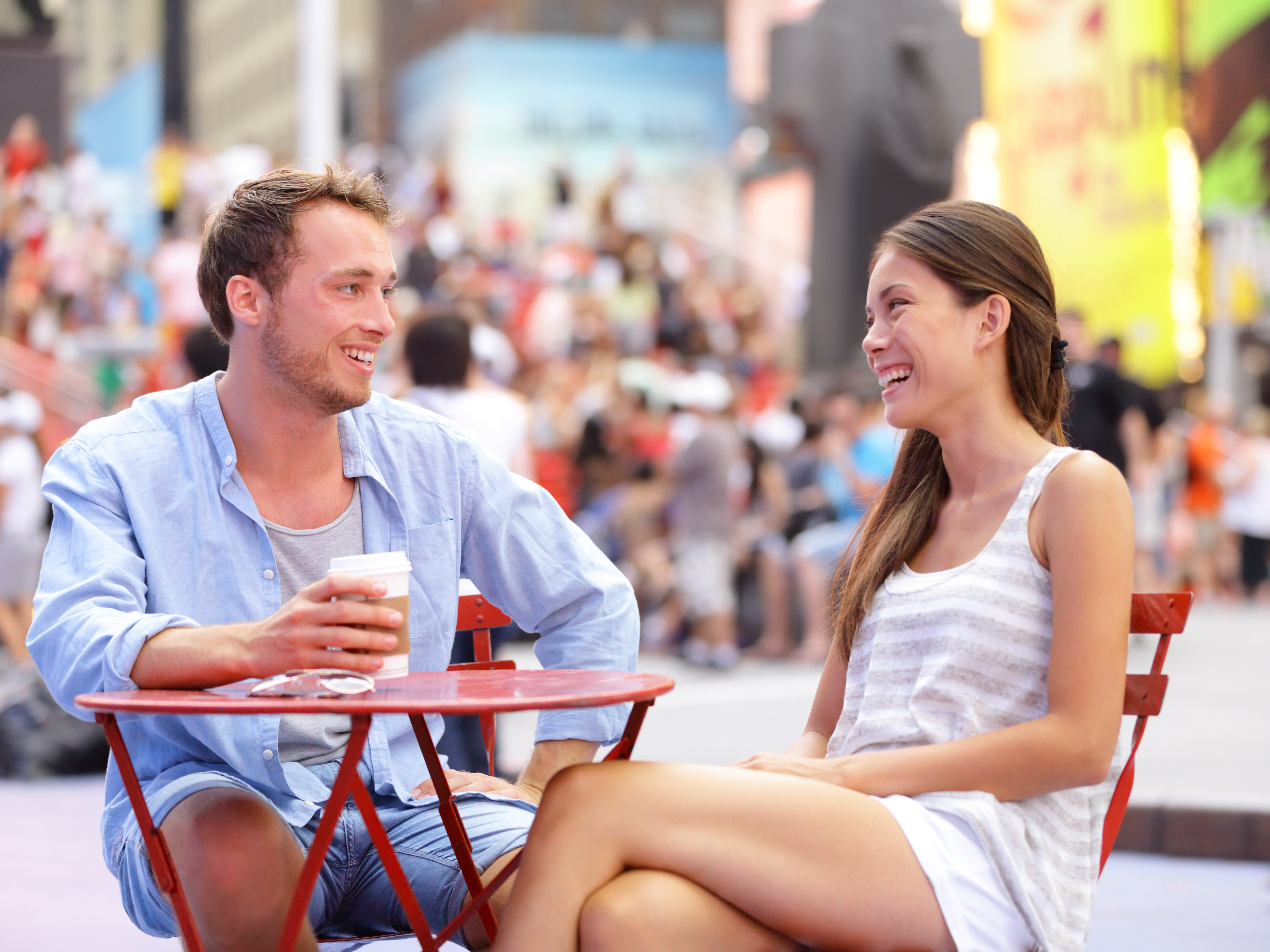 Dating couple, New York, Manhattan, Times Square dating drinking coffee smiling happy sitting at red tables enjoying their tourism vacation travel in the USA. Asian woman, Caucasian man.
